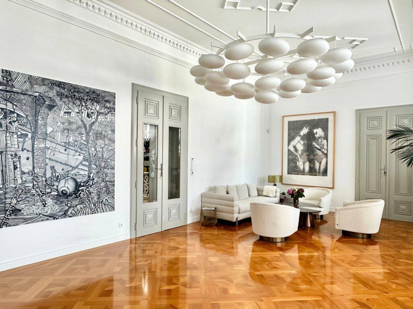 Geräumiger Wohnbereich mit glänzendem Parkettboden, Stuckdecken und moderner Kunst an den Wänden.