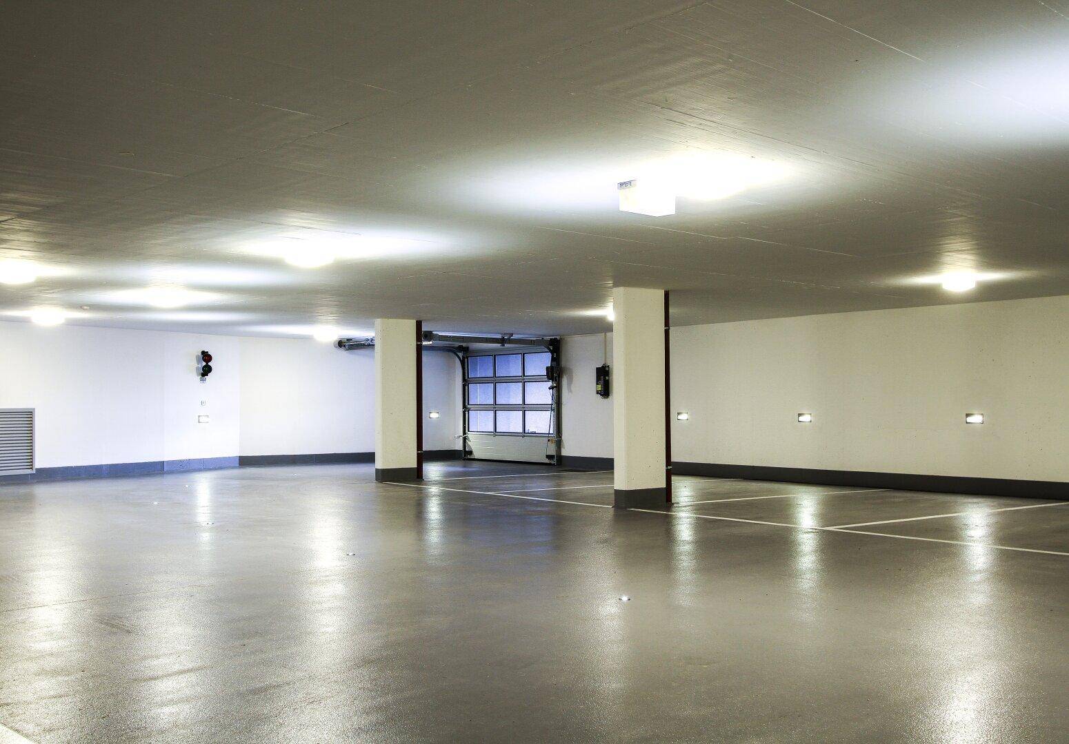 Geräumige Tiefgarage mit vielen Stellplätzen, heller Beleuchtung und klaren Fahrbahnmarkierungen.