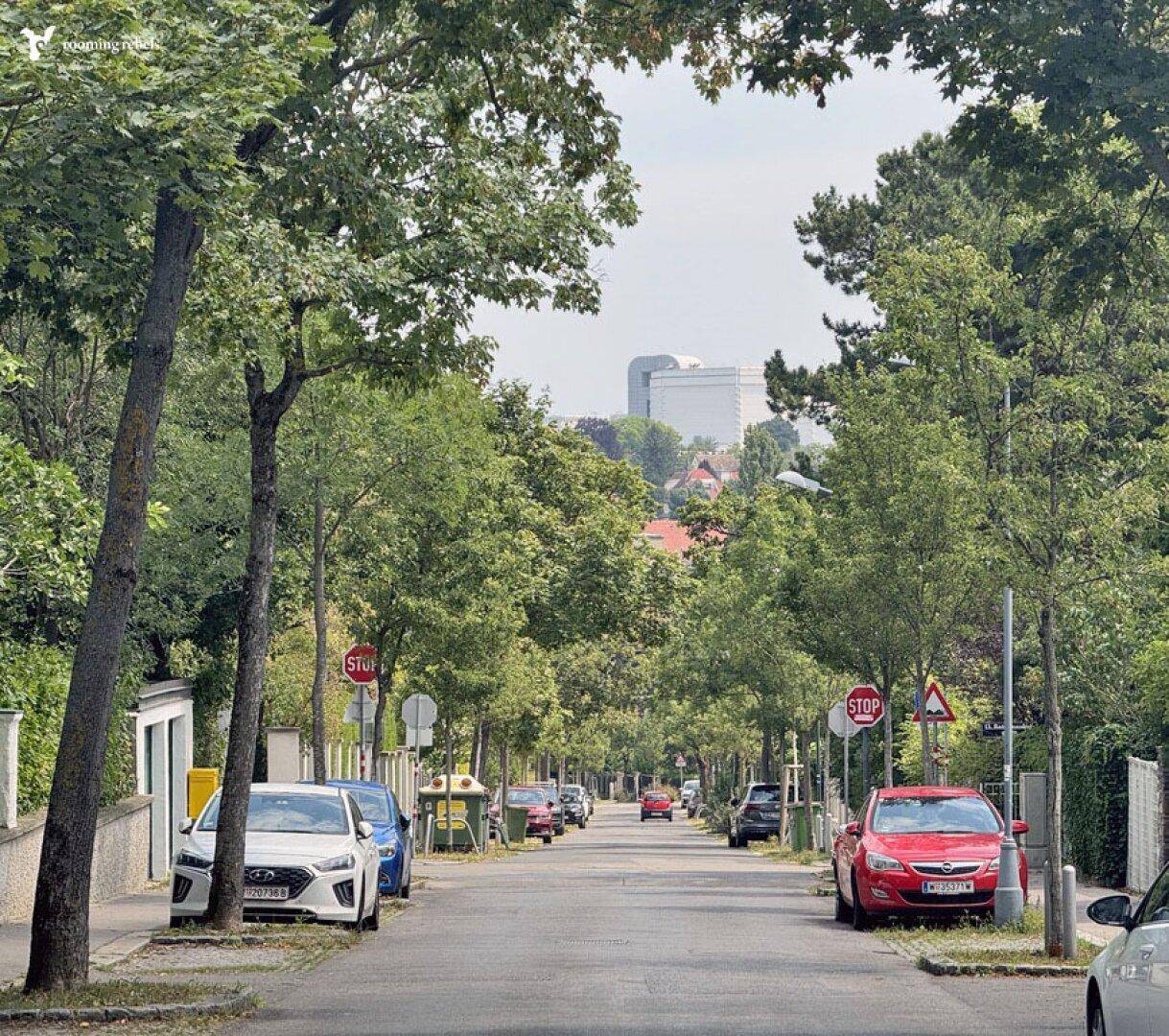 Eine von Bäumen gesäumte Wohnstraße mit geparkten Autos und einem Gebäude in der Ferne.