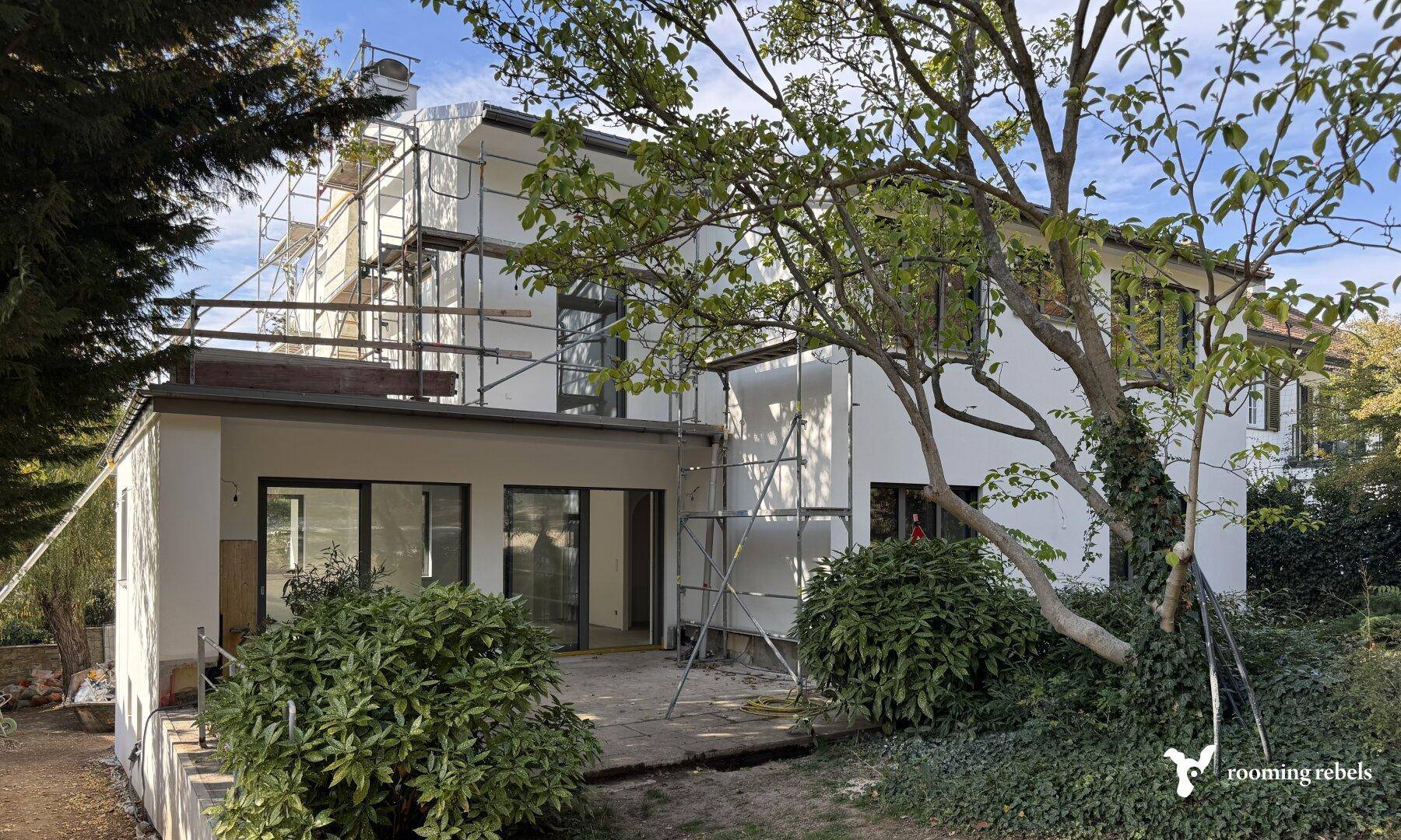 Ein Haus im Umbau mit Gerüst an der Fassade und einer Terrasse im Erdgeschoss.