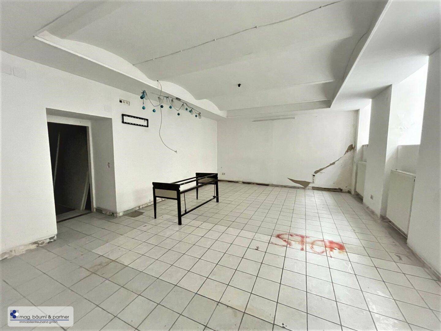 Geräumiger, leerer Gewerberaum mit Fliesenboden und hohen Decken, bereit für die Neugestaltung.