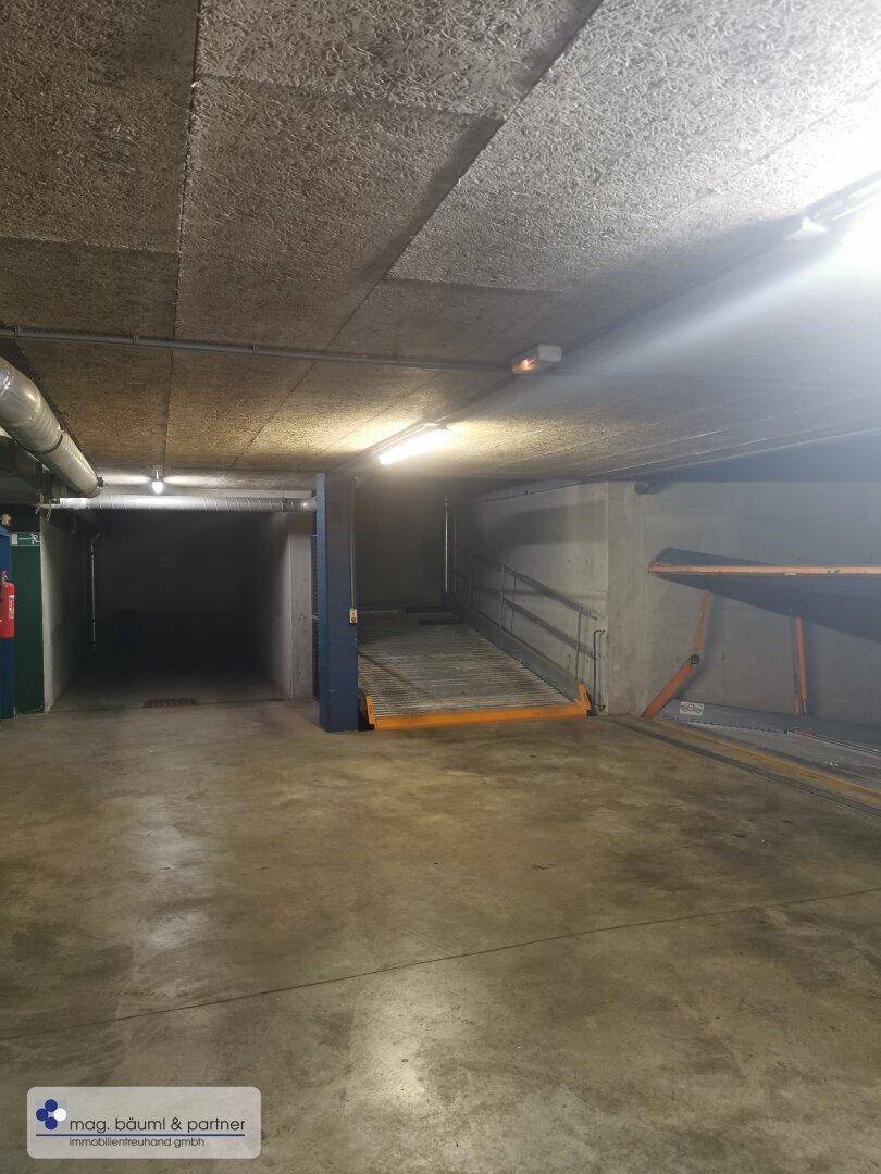 Geräumige Tiefgarage mit einem Doppelparker-System und Betonoberflächen an Decke und Wänden.