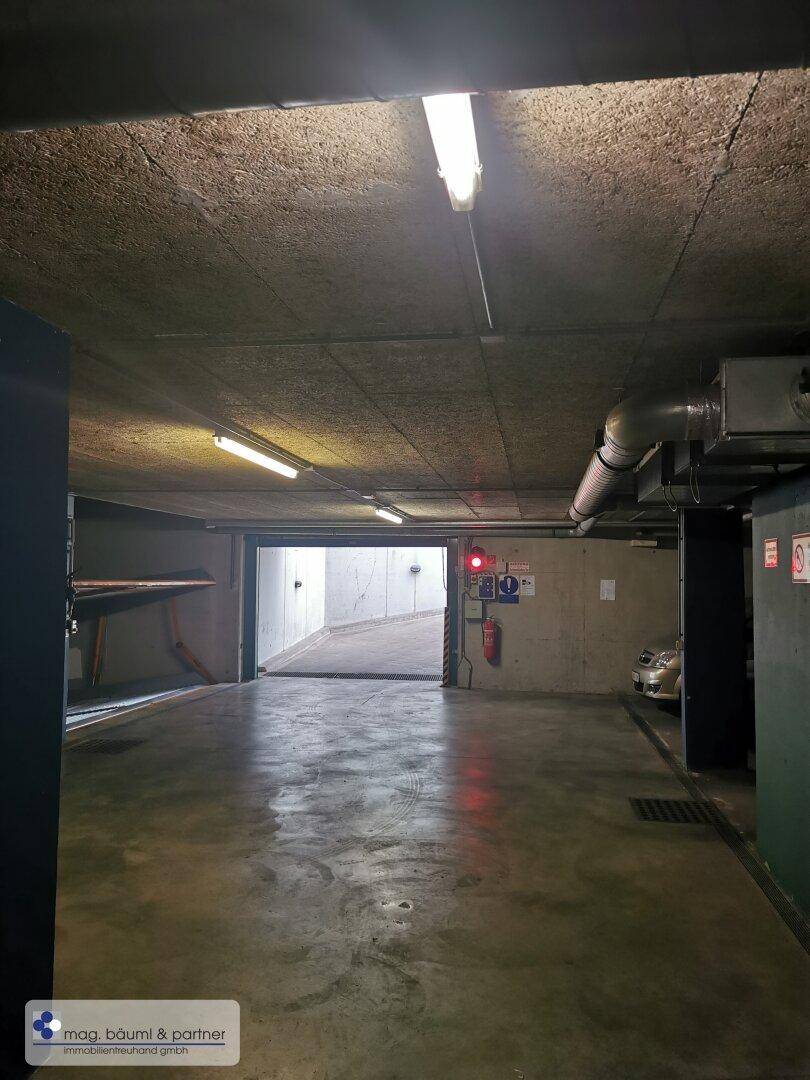 Blick in die Tiefgarage mit Betonwänden und Decken, beleuchtet von Leuchtstoffröhren.