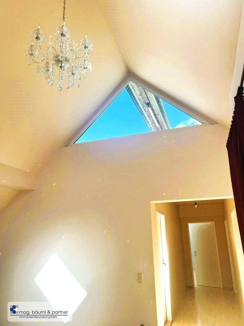 Heller Raum mit großem dreieckigem Fenster und Kronleuchter, der viel natürliches Licht hereinlässt.