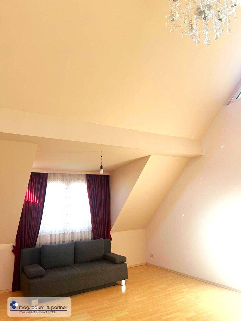 Heller Raum mit Dachschräge, einem bequemen Sofa und Parkettboden, der eine gemütliche Atmosphäre schafft.