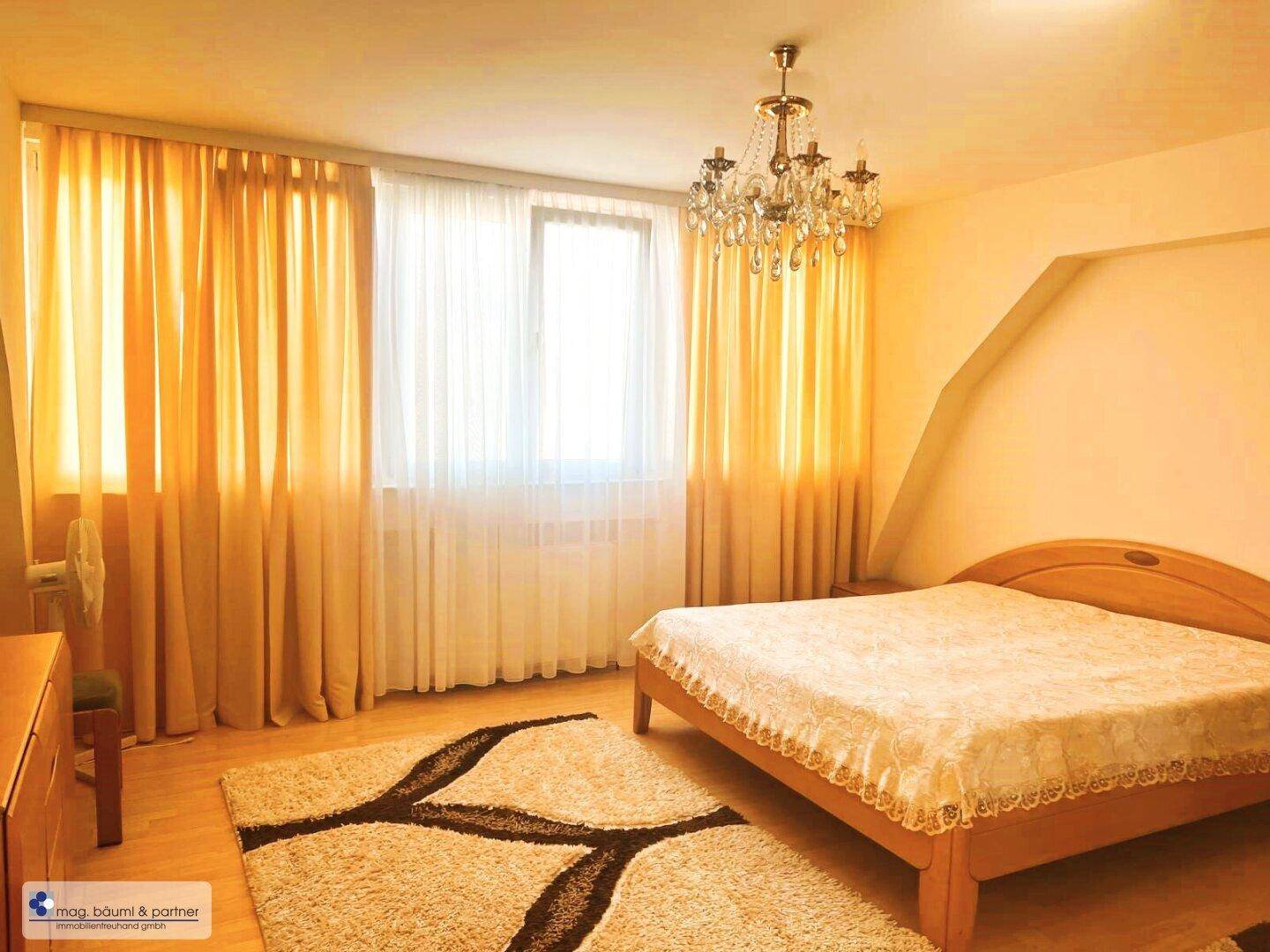 Helles Schlafzimmer mit Holzbett, Parkettboden und gelben Vorhängen, gut beleuchtet durch das Fenster.