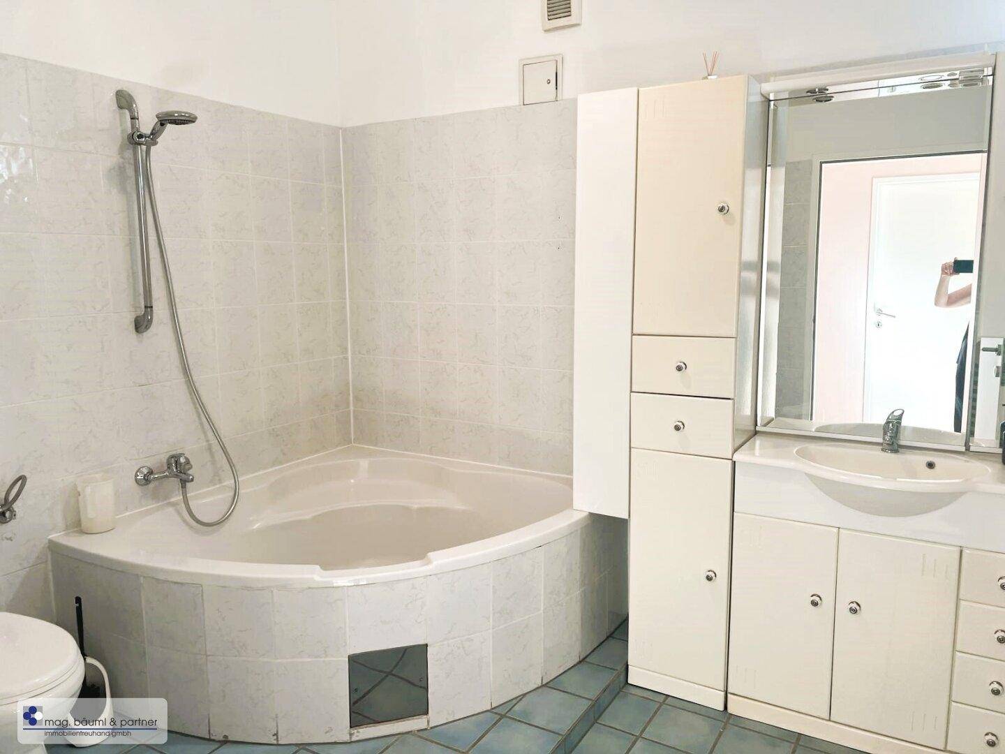 Badezimmer mit Eckbadewanne, Waschbecken und Spiegelschrank, ausgestattet mit hellen Fliesen.