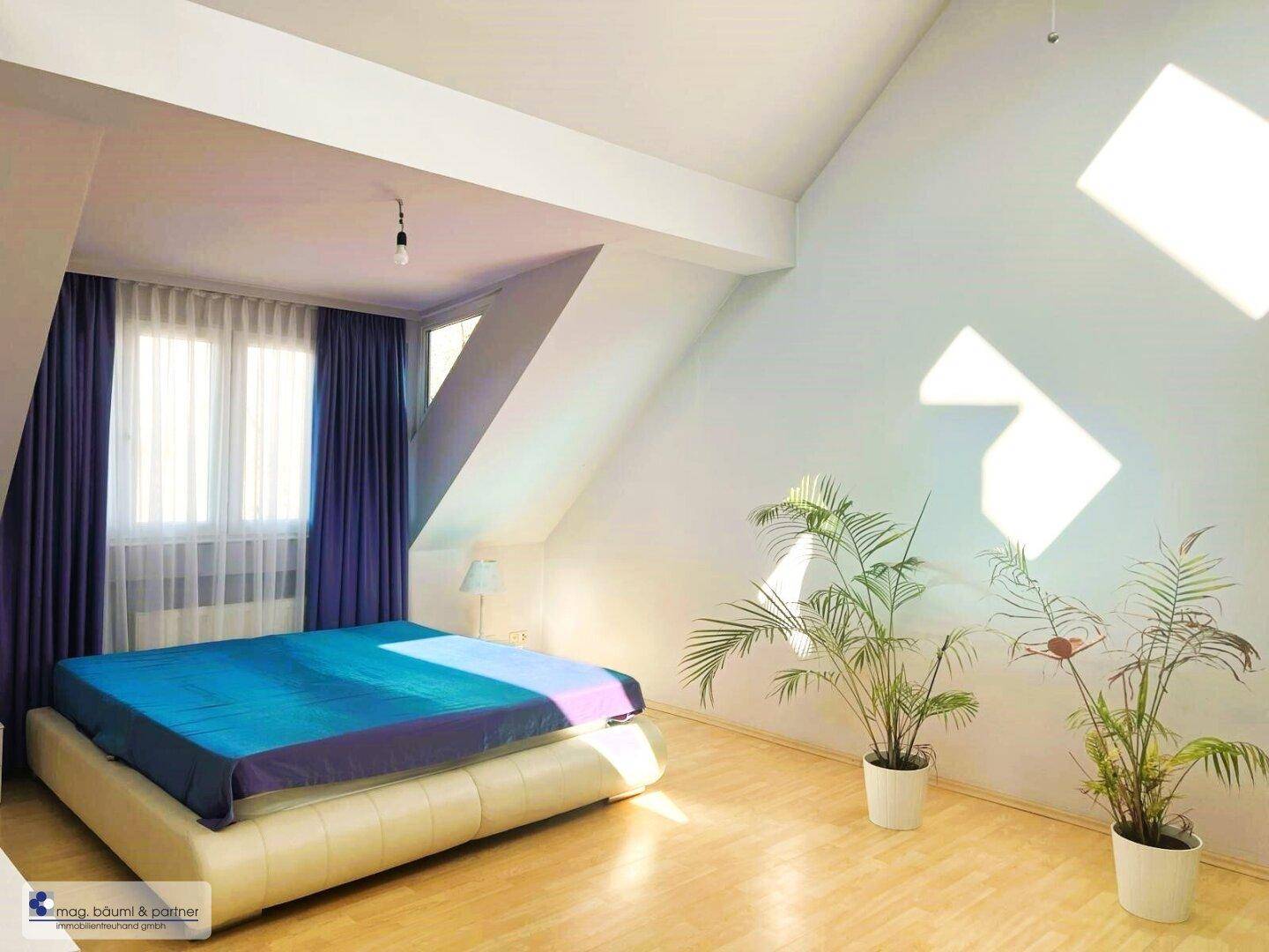Lichtdurchflutetes Schlafzimmer mit Dachschräge, Parkettboden und Zimmerpflanzen, die eine frische Atmosphäre schaffen.
