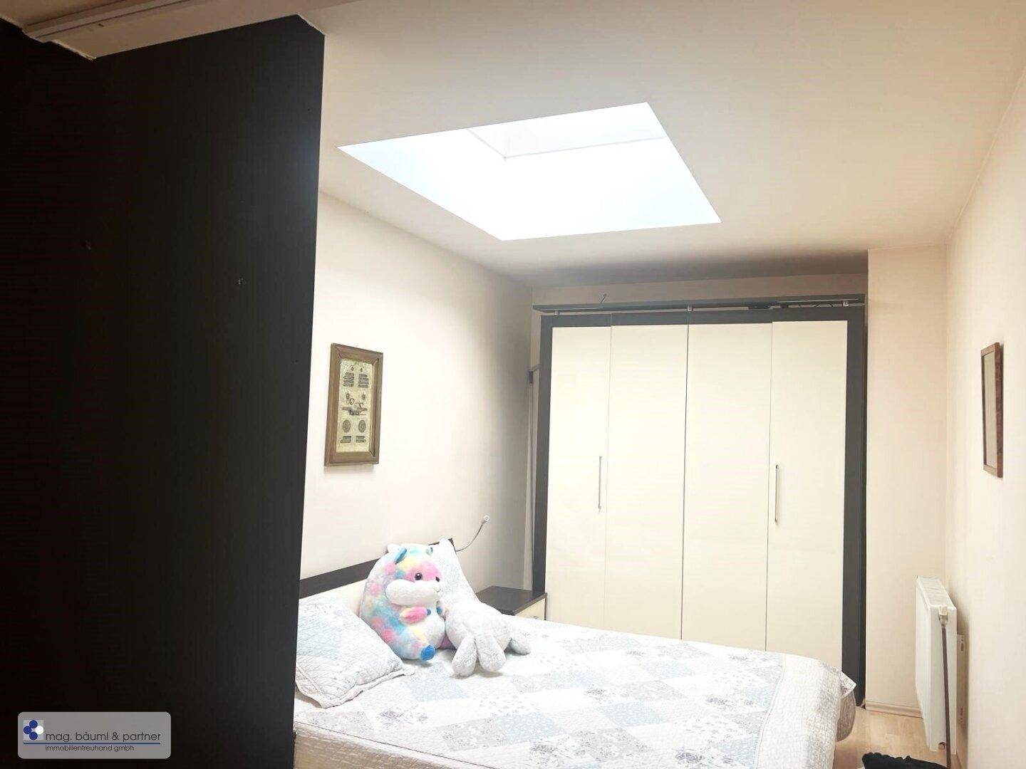 Schlafzimmer mit Einbauschrank, Bett und einem Oberlicht, das für natürliches Tageslicht sorgt.