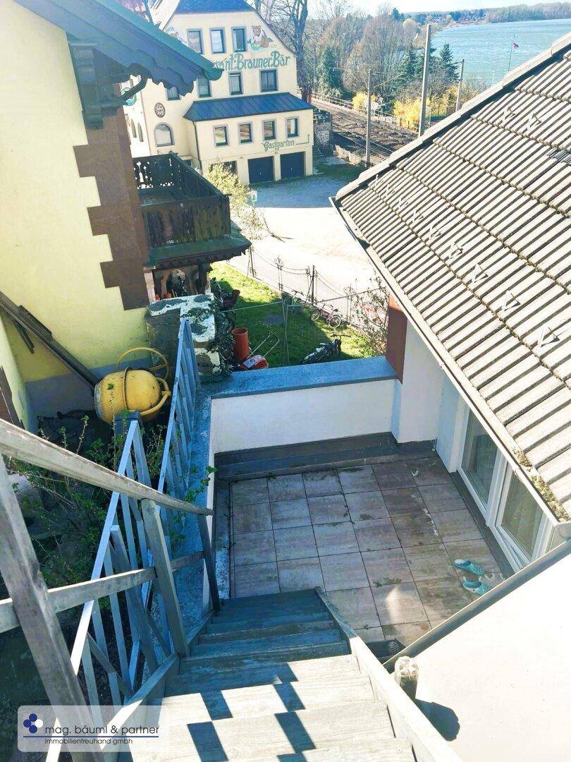 Untere Terrasse mit Fliesenboden und Holztreppe, die zu weiteren Bereichen führt, mit Blick auf die Umgebung.