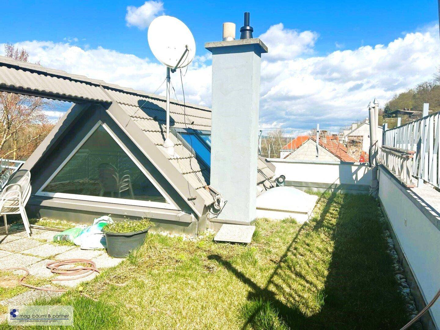 Dachterrasse mit Rasenfläche, einem Kamin und Satellitenschüssel, umgeben von einer malerischen Landschaft.