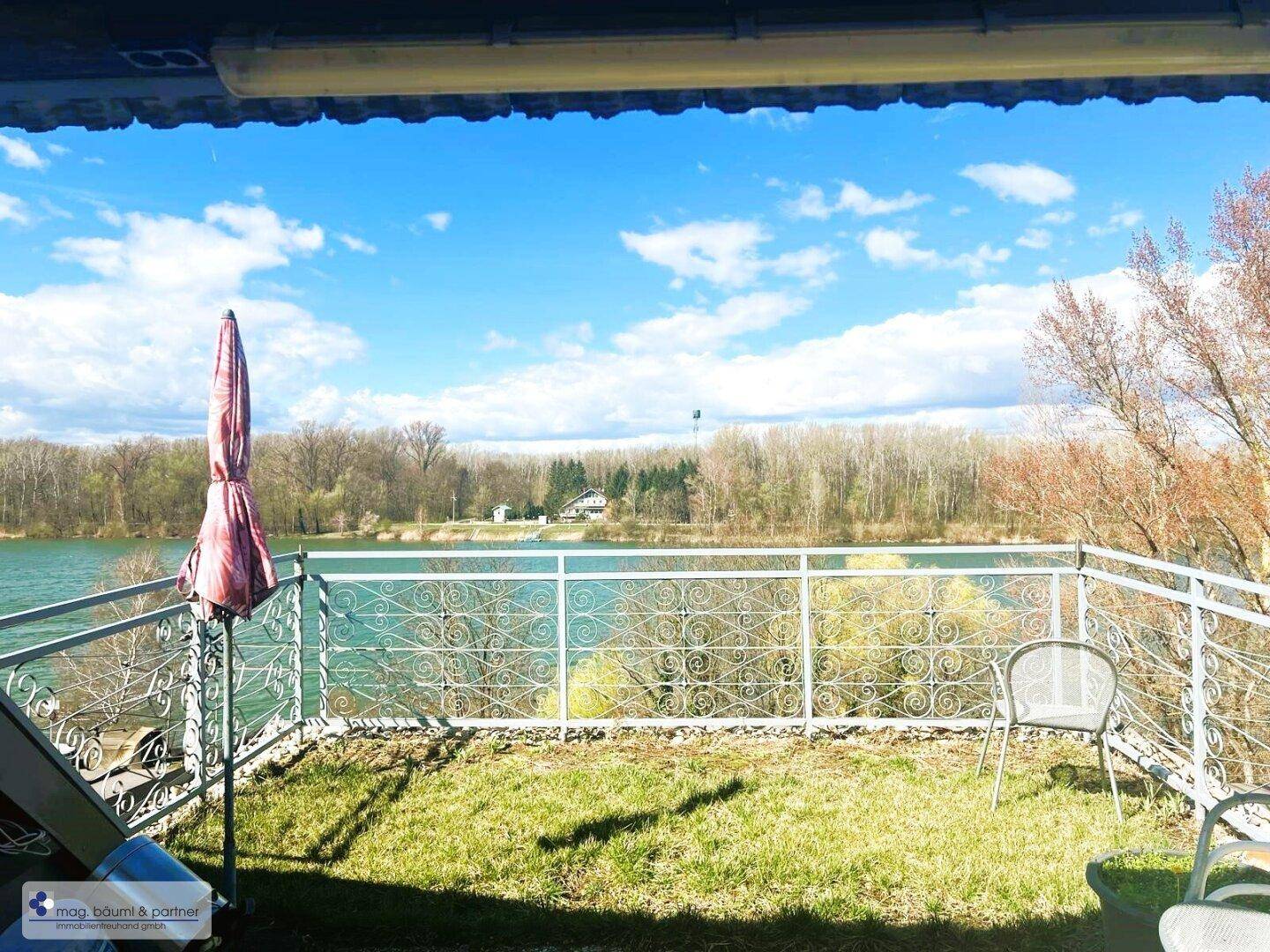 Sonnige Terrasse mit Seeblick, Gartenmöbeln und Sonnenschirm, ideal zum Entspannen im Freien.