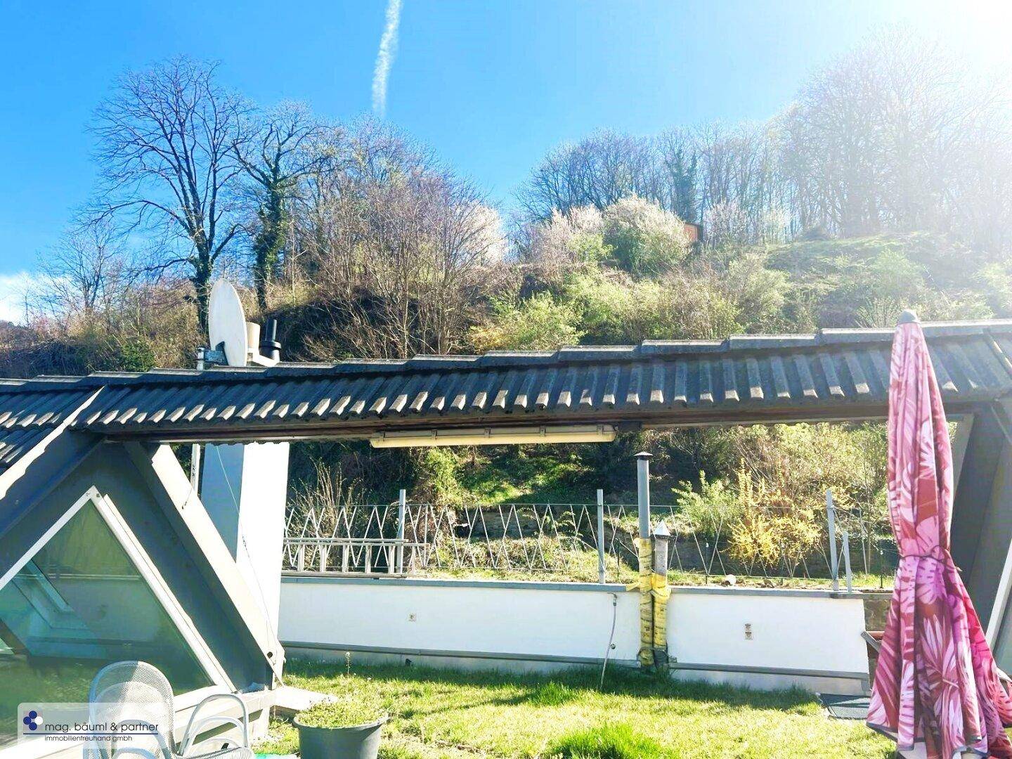 Dachterrasse mit Blick auf den bewaldeten Hügel und Sonnenschirm, bietet eine ruhige und grüne Aussicht.