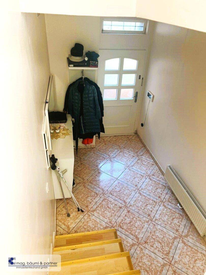 Eingangsbereich mit Fliesenboden, Garderobe und einer Holztreppe, die in die oberen Etagen führt.