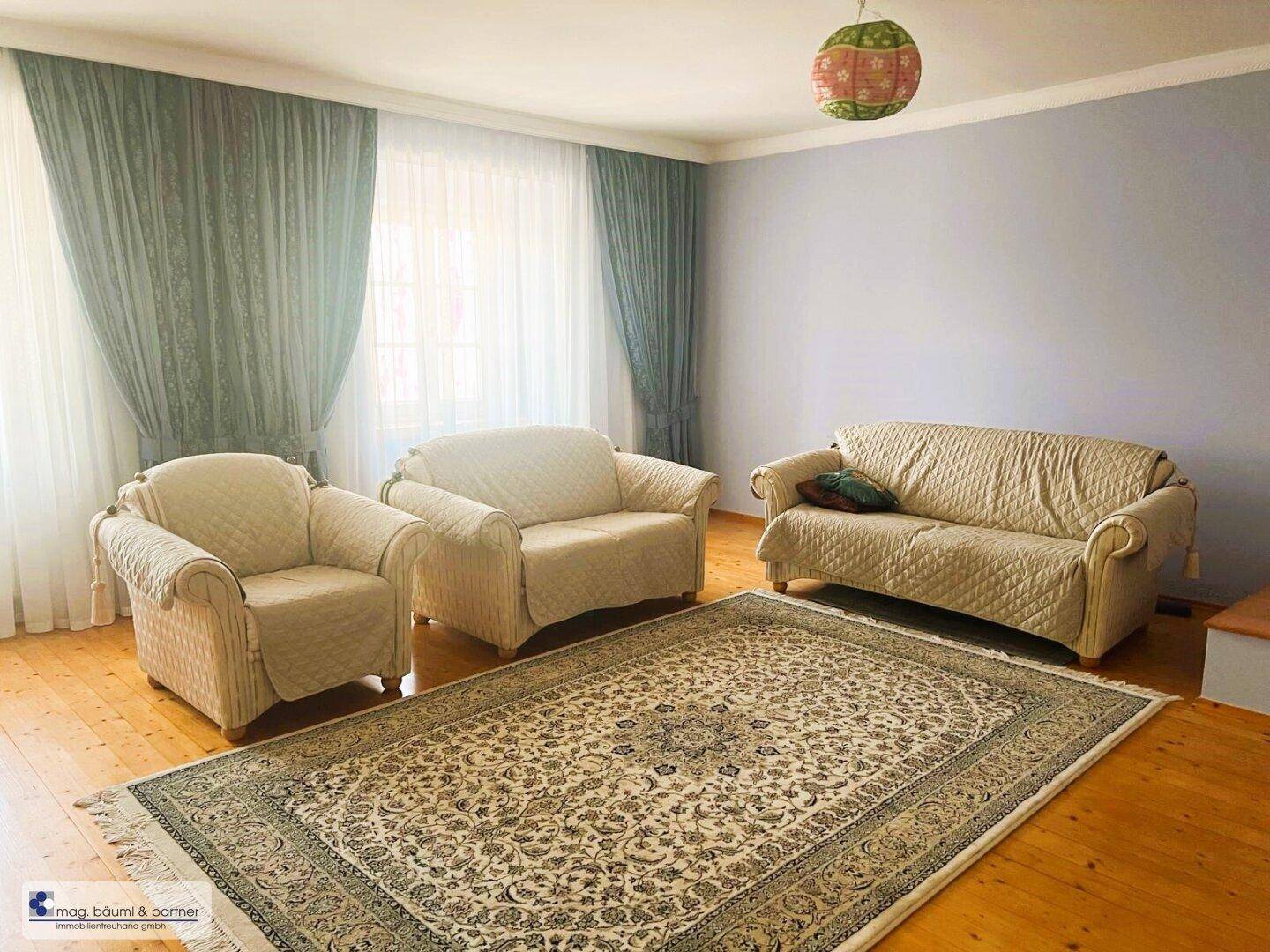 Wohnzimmer mit beigen Sofas, Parkettboden und einem gemusterten Teppich, der den Raum gemütlich macht.