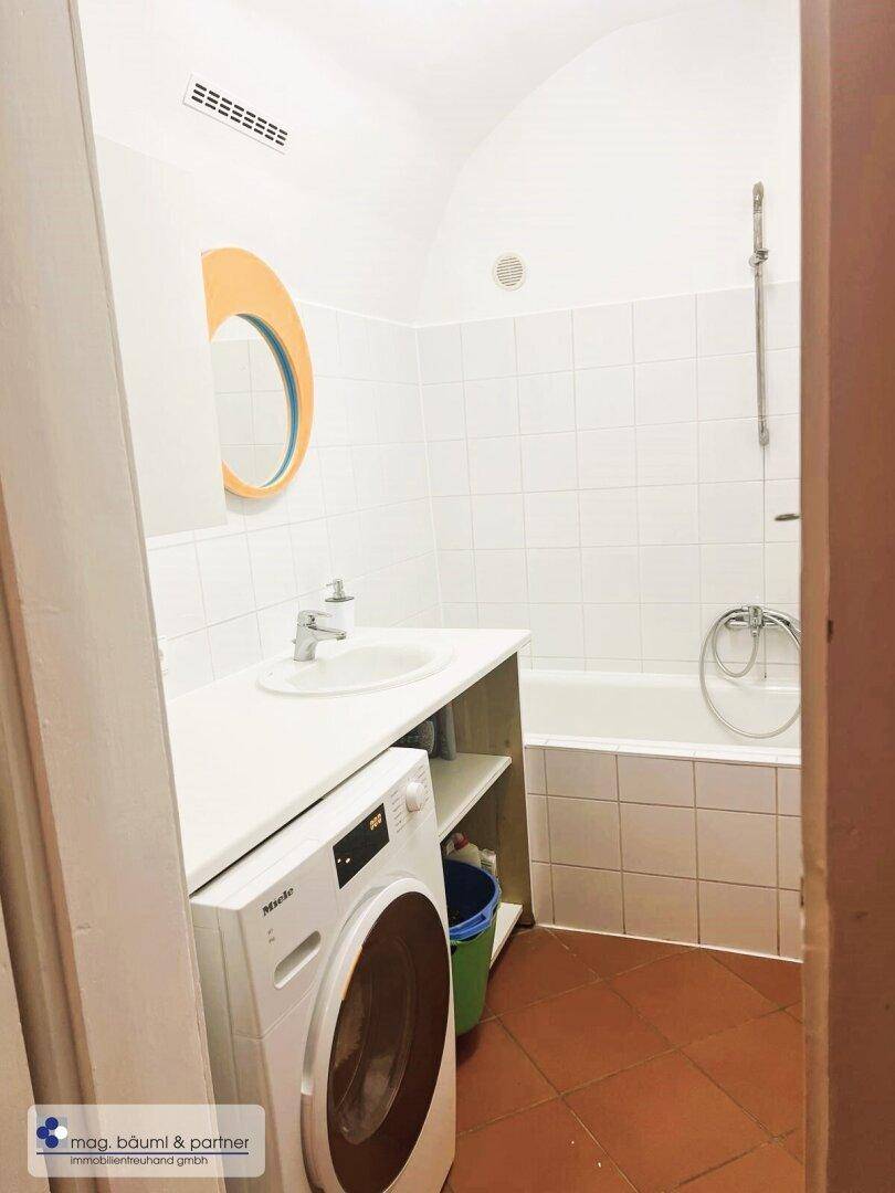 Badezimmer mit Badewanne, Waschbecken und einer Waschmaschine, praktisch und funktional eingerichtet.
