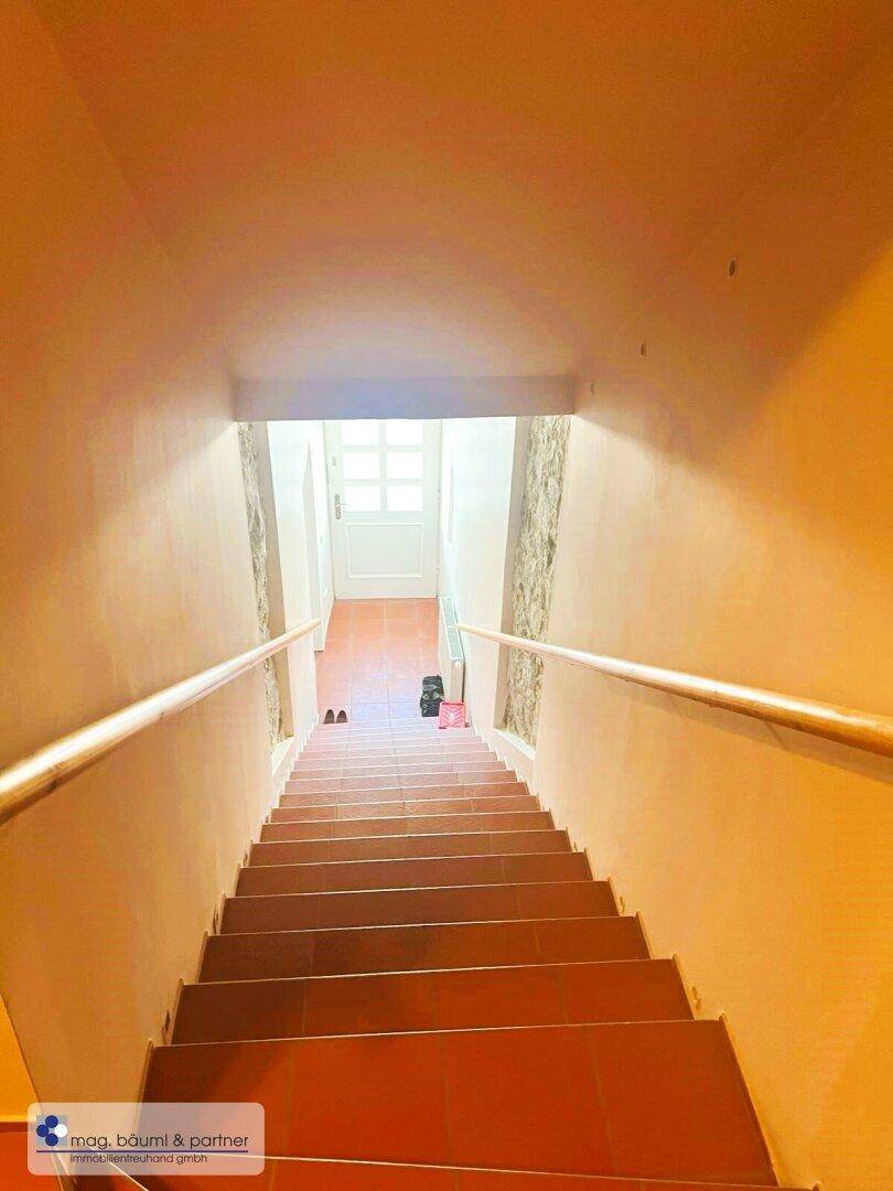 Langer Treppenabgang mit Fliesenboden und Handläufen, der in die untere Etage führt.