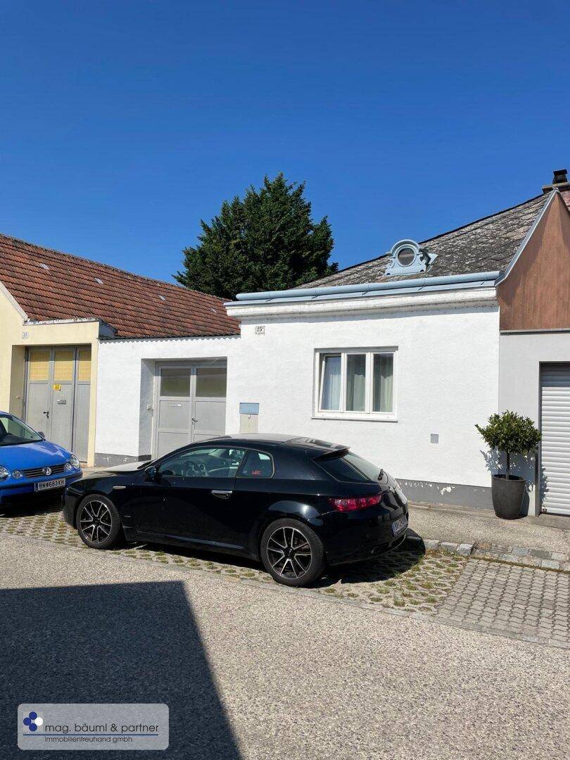 Fassade eines weißen Hauses mit einem schwarzen Sportwagen davor auf der Straße.
