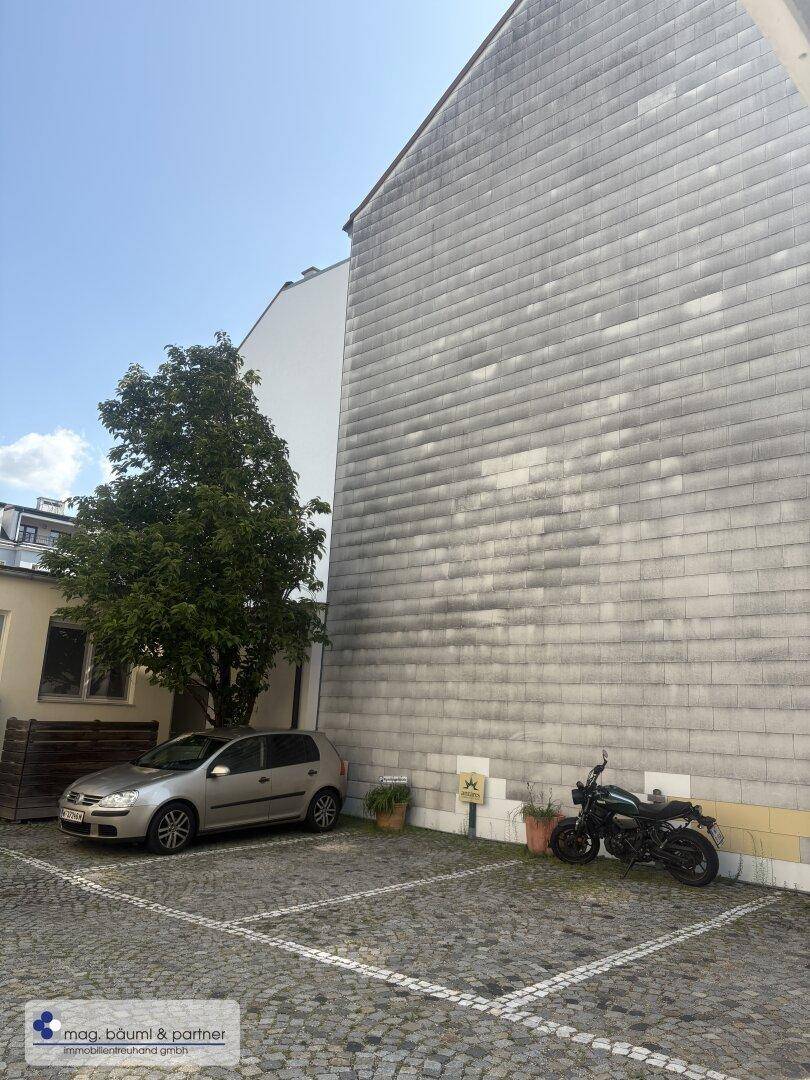 Seitenansicht eines Gebäudes mit großer, schlichter Fassade und gepflastertem Parkplatz.