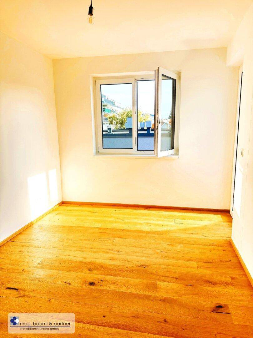 Helles Schlafzimmer mit Holzboden und einem großen Fenster, das viel Tageslicht hereinlässt.