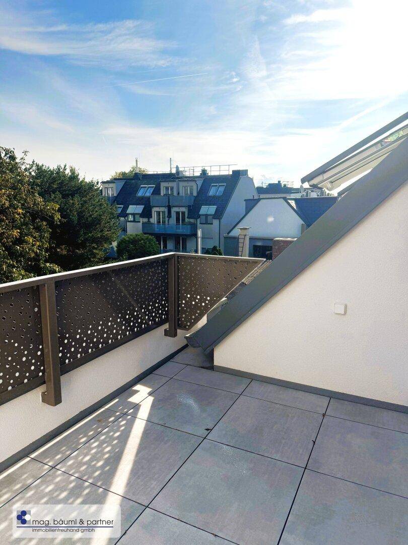 Sonniger Terrassenbereich mit modernen Fliesen und Blick auf die umliegenden Gebäude.