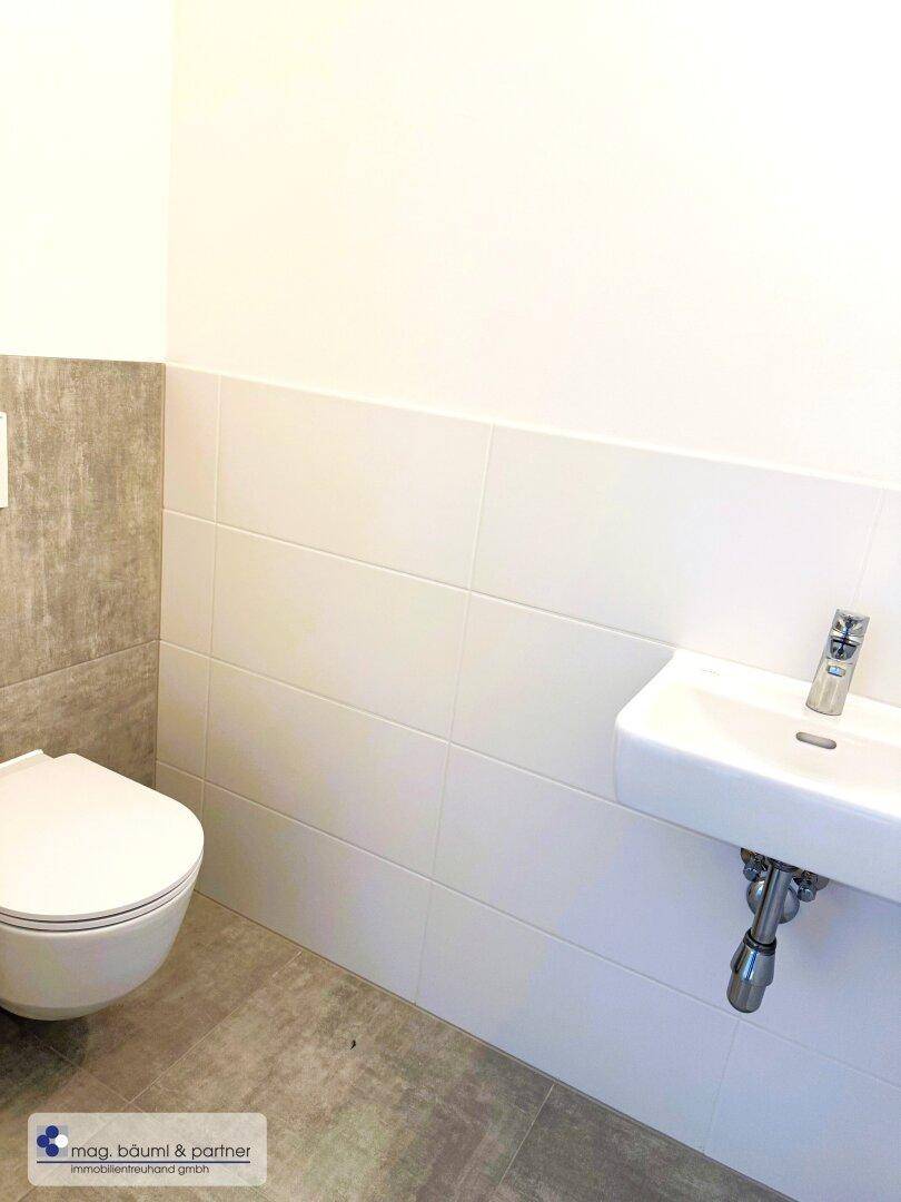 Modernes Gäste-WC mit wandhängender Toilette und kleinem Waschbecken in neutralen Farben.