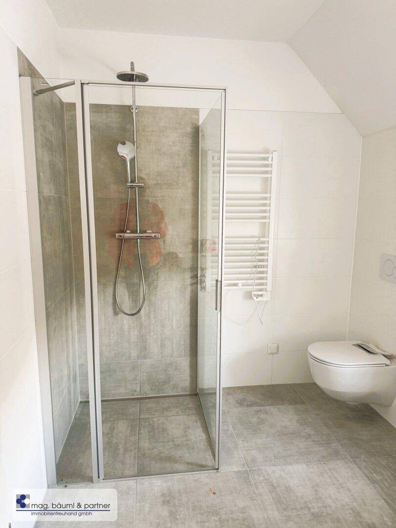 Modernes Badezimmer mit Duschkabine, wandhängender Toilette und beheiztem Handtuchhalter.