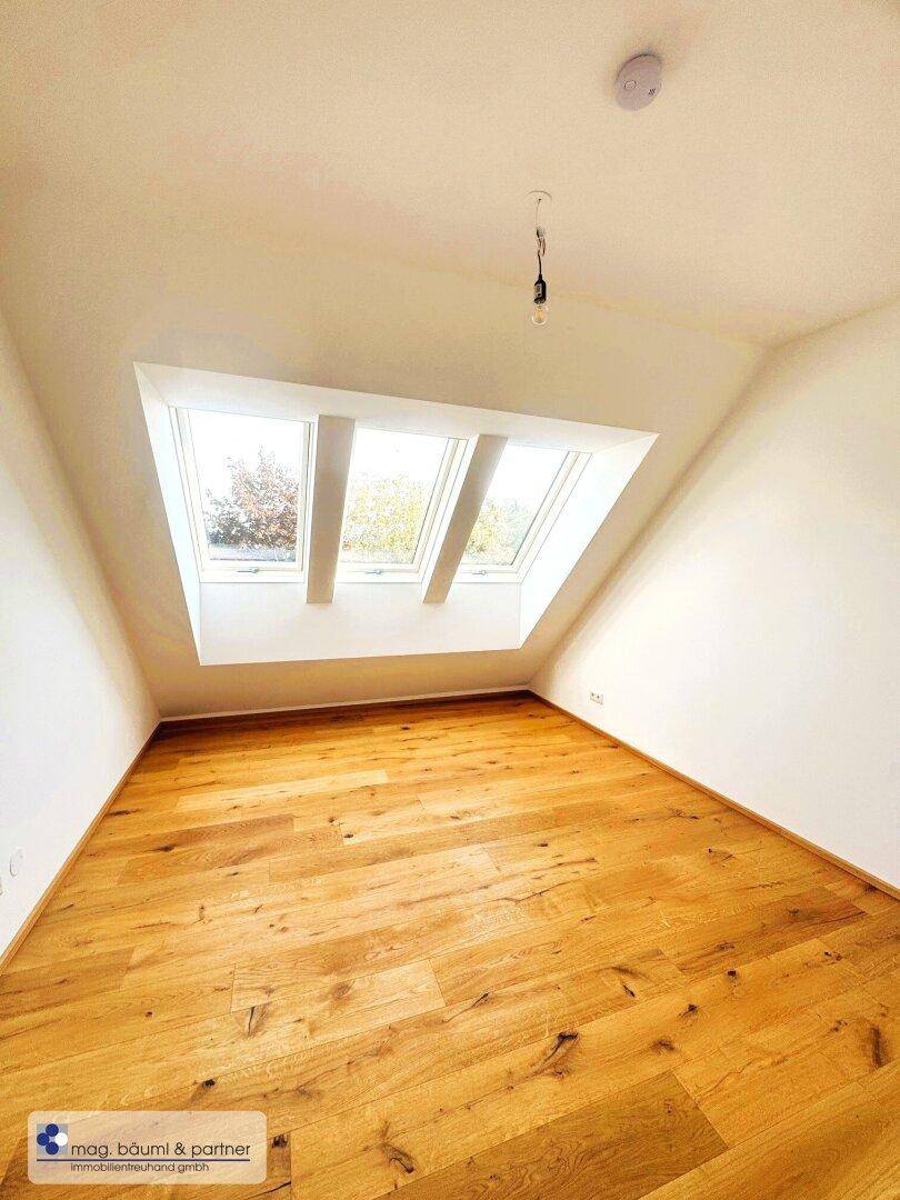 Dachgeschosszimmer mit Holzboden, schrägen Wänden und drei Dachfenstern für viel Licht.