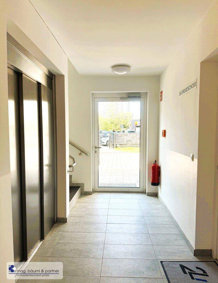 Heller Eingangsbereich mit Fliesenboden, modernem Aufzug und Zugang zum Treppenhaus.
