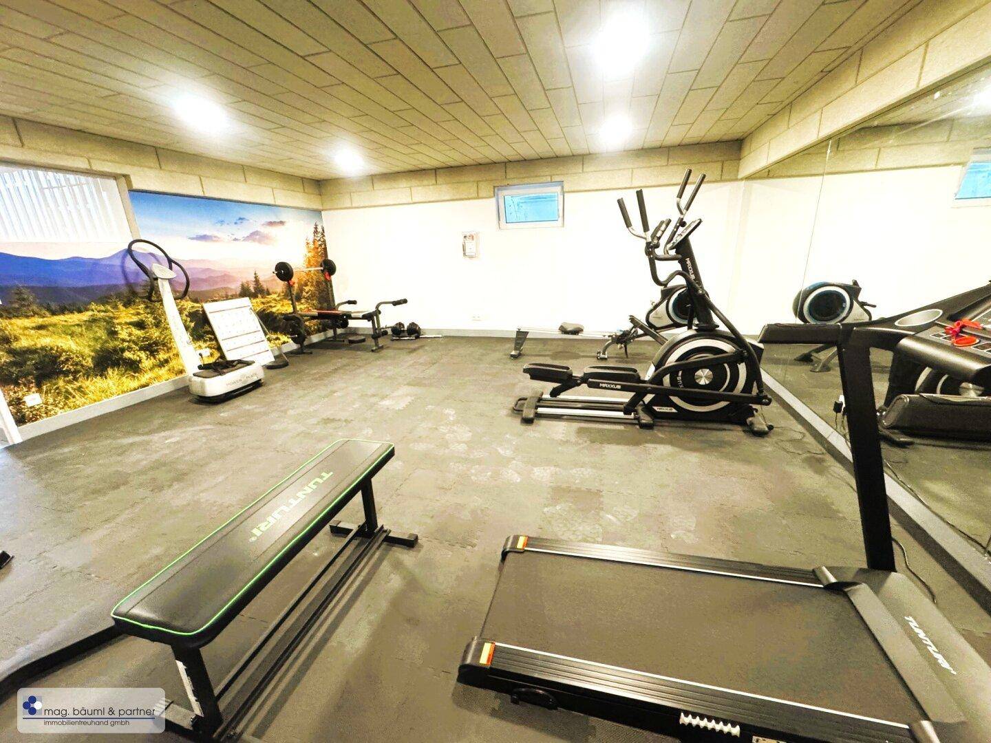 Geräumiger Fitnessbereich mit Laufband, Crosstrainer und großem Spiegel für das Training.