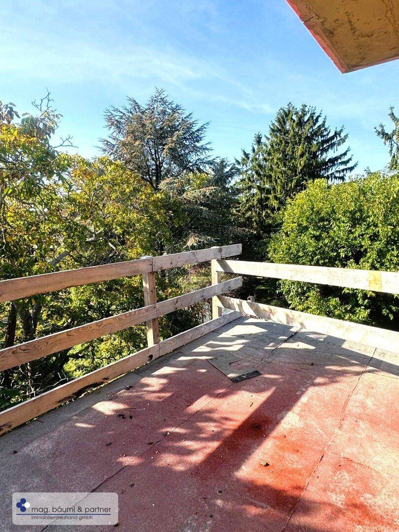 Unfertige Terrasse mit Holzzaun und Blick ins Grüne unter blauem Himmel.
