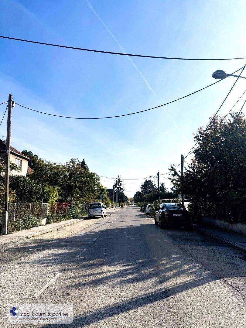 Ruhige Wohnstraße mit geparkten Autos und Häusern unter klarem blauem Himmel.