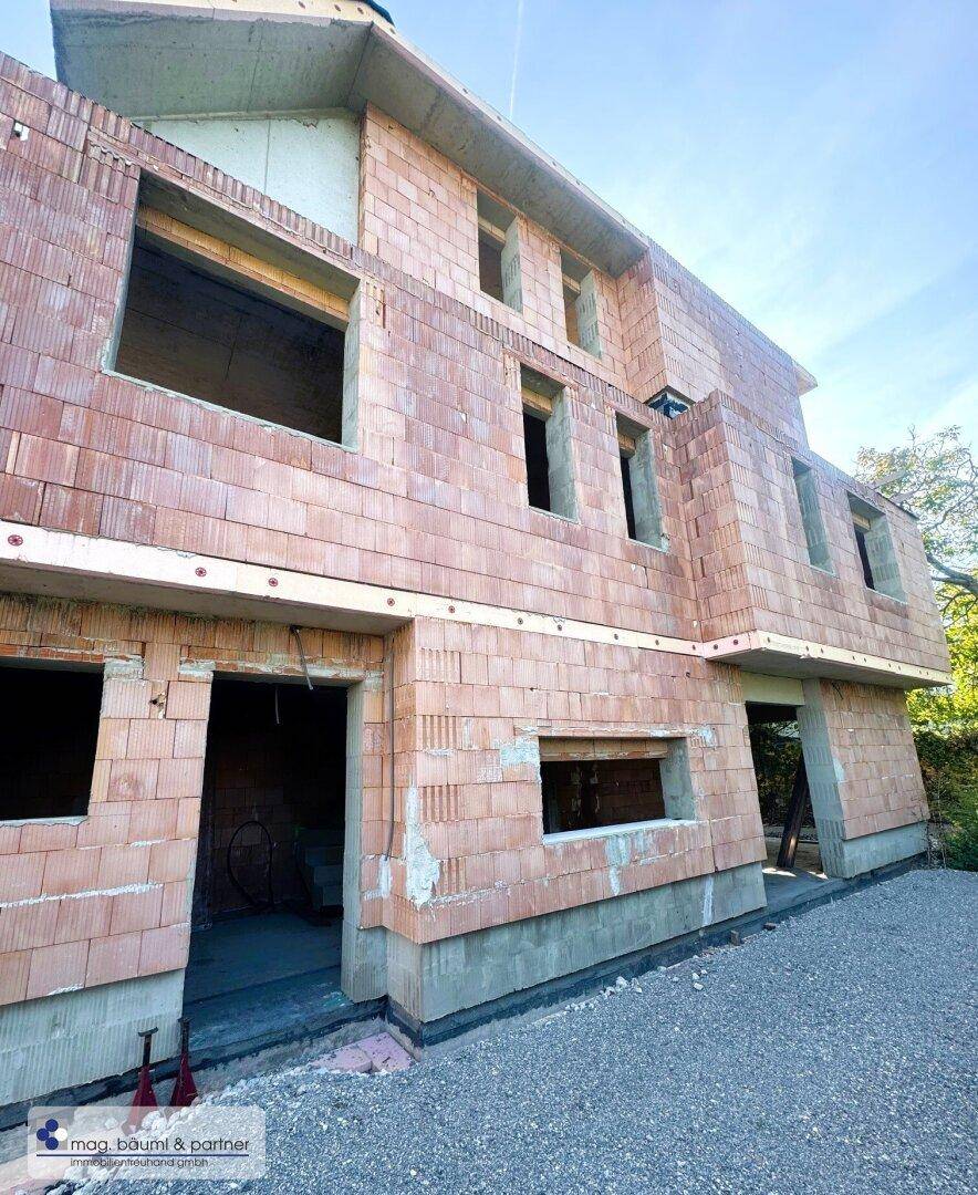 Außenansicht eines im Bau befindlichen Hauses mit Ziegelwänden und Fensteröffnungen.