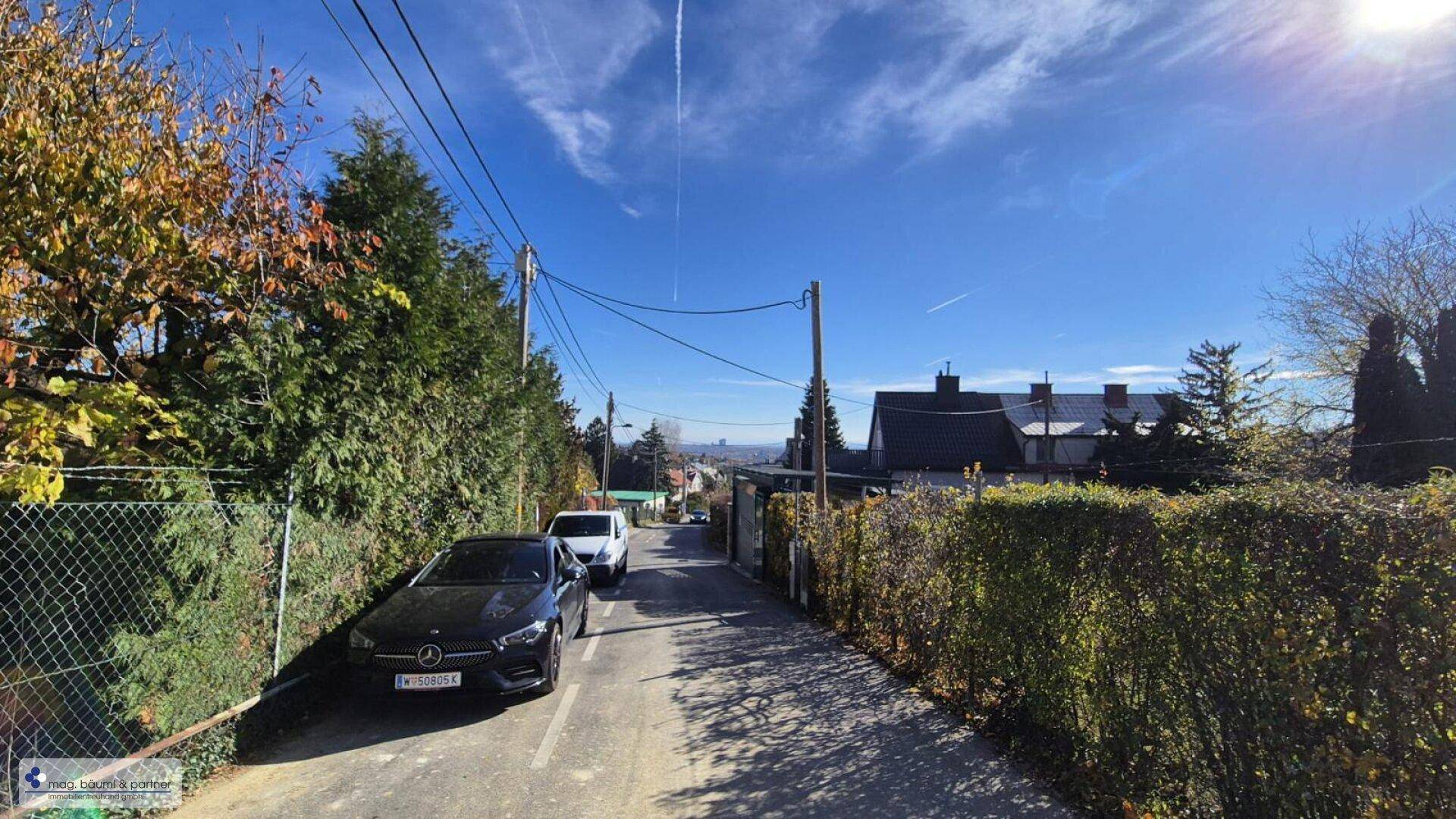 Ruhige Wohnstraße mit parkenden Autos und Blick auf die umliegende Landschaft.