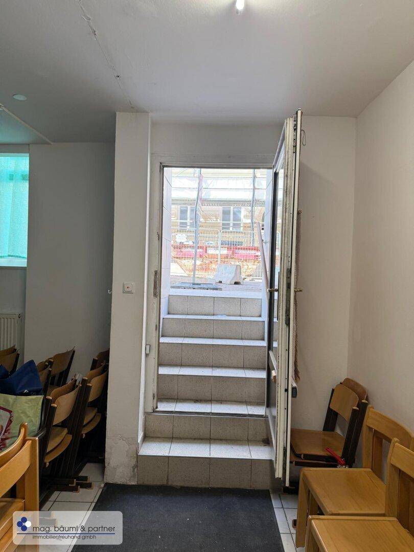 Eingangsbereich mit gefliesten Stufen, die zu einer Außentür führen, umgeben von einfachen Wänden.