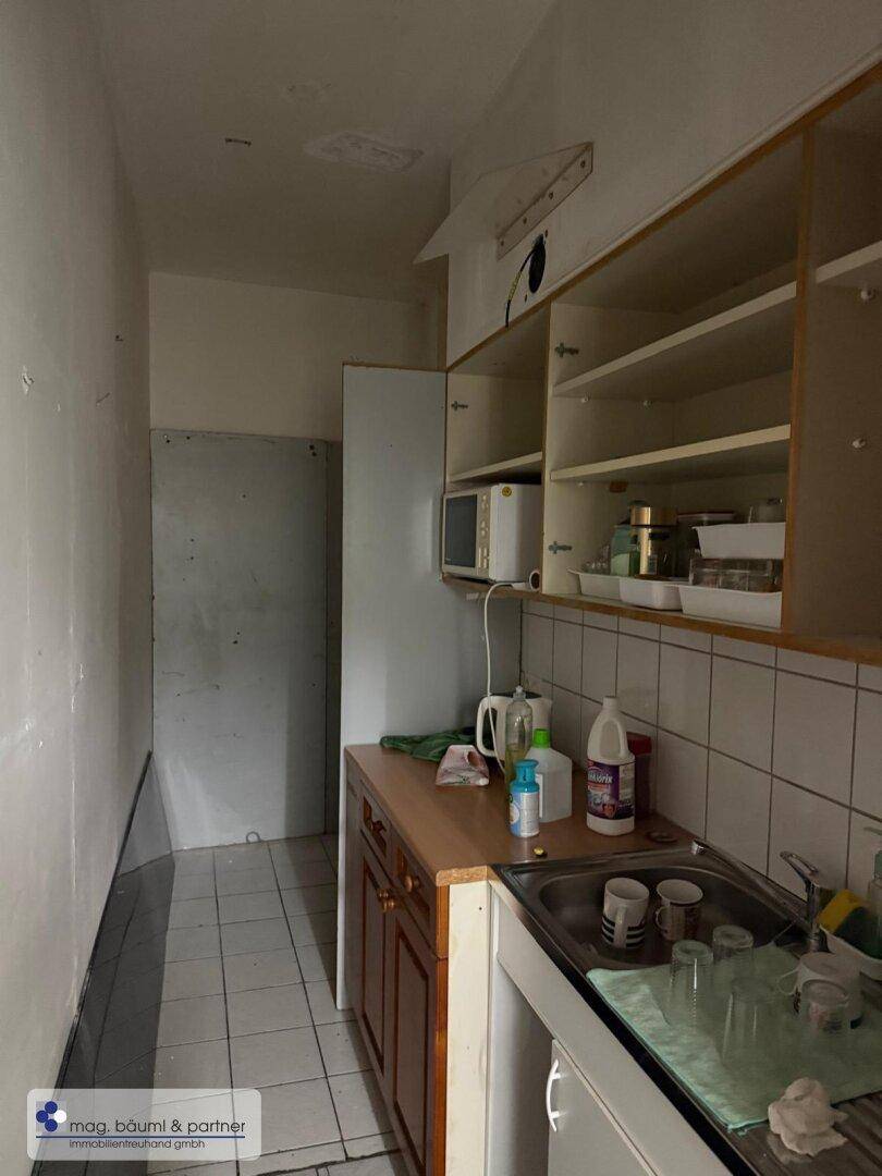 Kleine Küche mit einfachen Holzschränken, Spüle und Mikrowelle, in einem funktionalen Zustand.