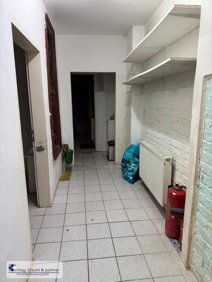 Langer Flur mit Fliesenboden, Heizkörper und Regalen an der Wand, der zu weiteren Räumen führt.