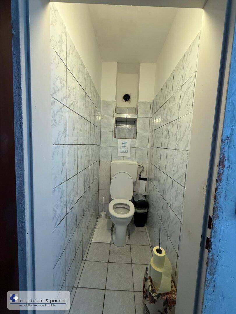 Kleiner Toilettenraum mit weißen Fliesen an Wänden und Boden, ausgestattet mit einer Standardtoilette.