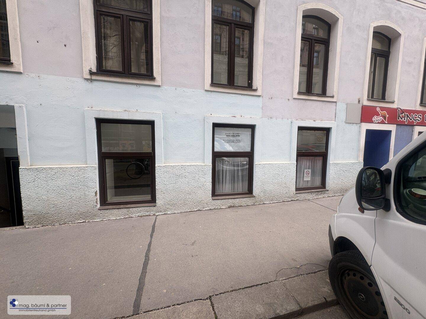 Gebäudefassade eines älteren Hauses mit mehreren Fenstern und einem Geschäft im Erdgeschoss, aufgenommen von der Straße.