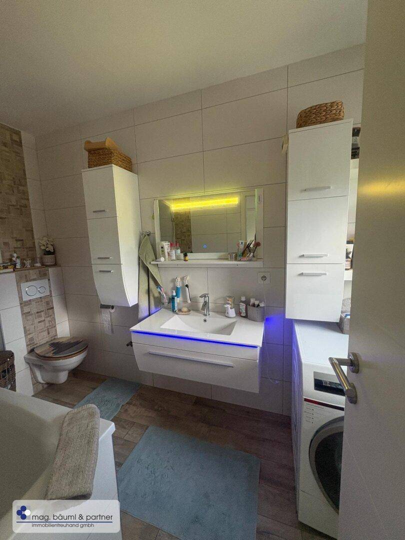 Modernes Badezimmer mit schwebendem Waschtisch, beleuchtetem Spiegel und integrierter Waschmaschine.