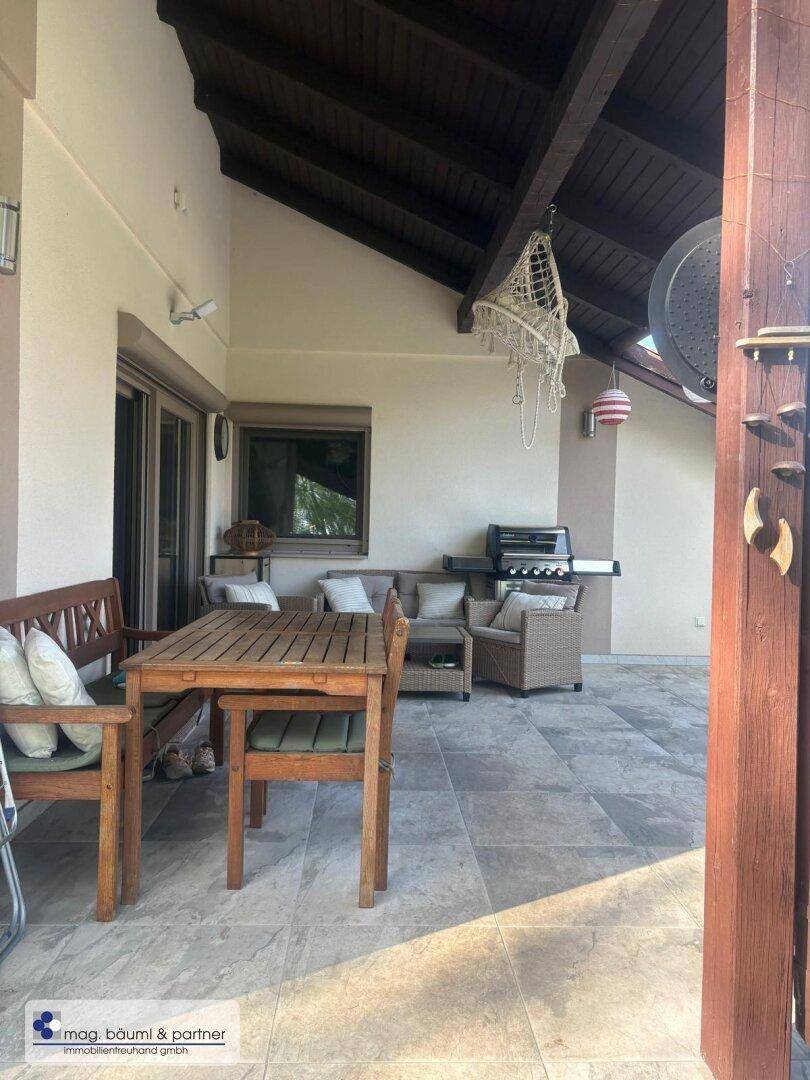 Überdachte Terrasse mit Holztisch, Sitzgelegenheiten und Grill, perfekt für Mahlzeiten im Freien.