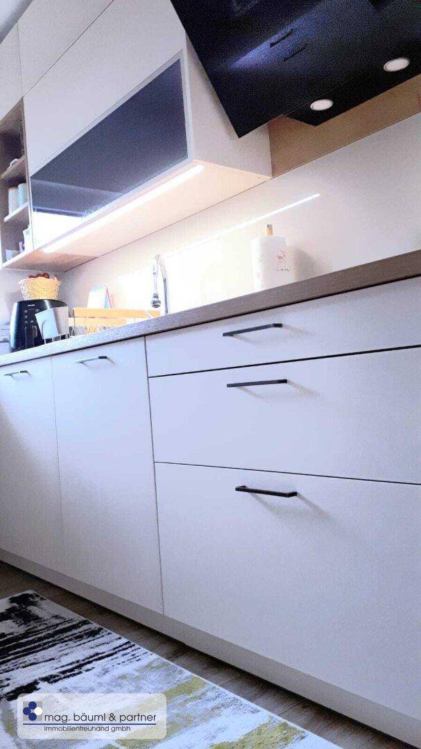 Detailansicht der modernen Küche mit weißen Schränken, Holztheke und integrierter Beleuchtung.