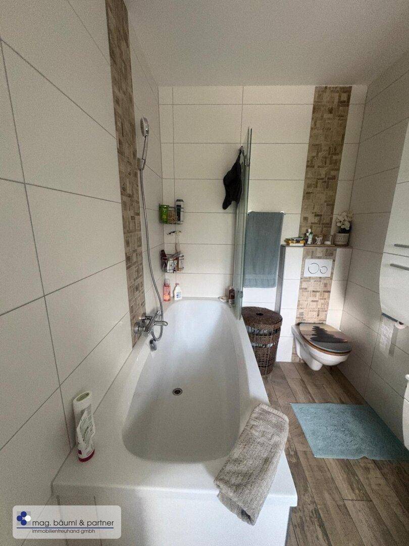 Badezimmer mit Badewanne, Wand-WC und modernen Fliesen in hellen Farbtönen.