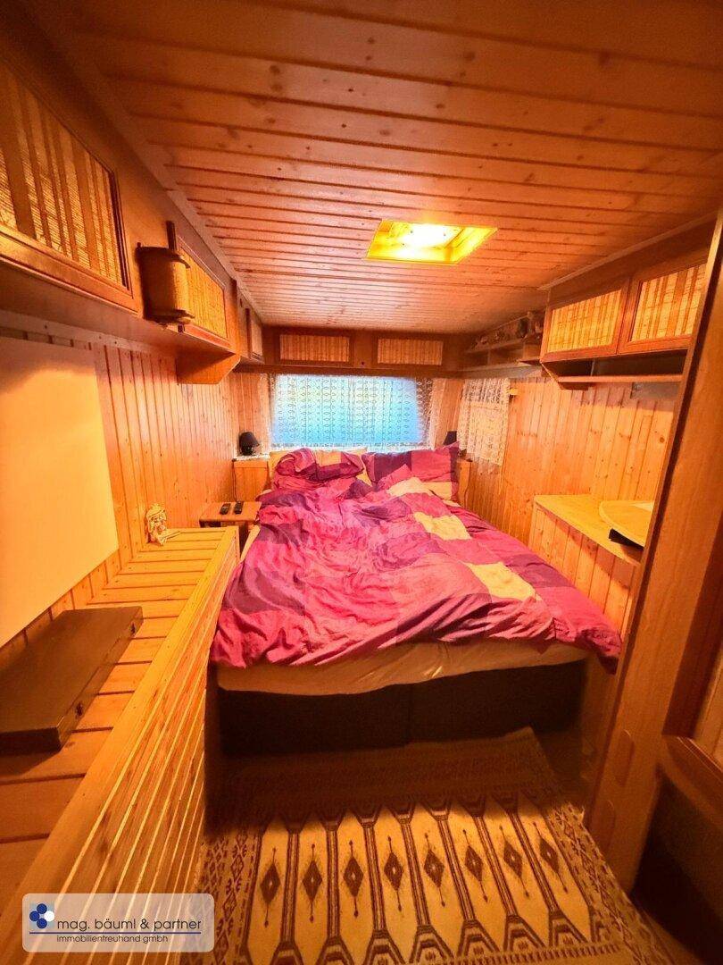 Schlafzimmer mit Holzvertäfelung, Doppelbett und Stauraum über dem Bett.
