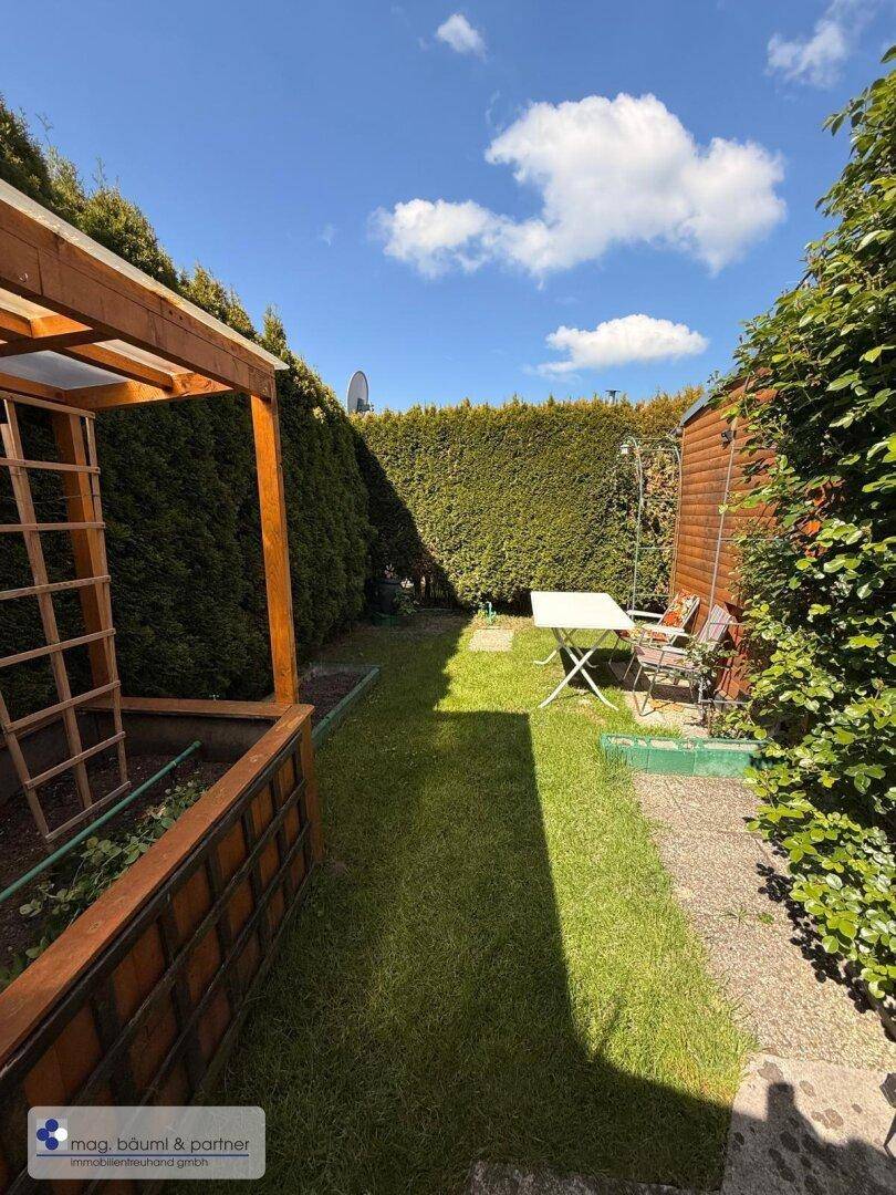 Langer Gartenbereich mit Rasen, hoher Hecke und Gartenhaus im Hintergrund.