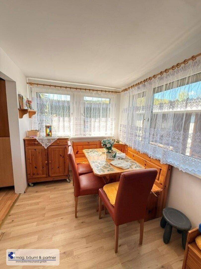 Gemütlicher Essbereich mit Holzeckbank, Esstisch und Fenstern mit Spitzenvorhängen.