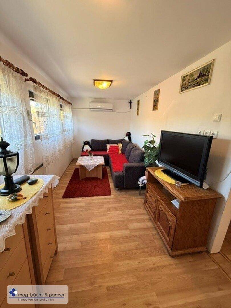Helles Wohnzimmer mit Laminatboden, rotem Sofa und Klimaanlage.