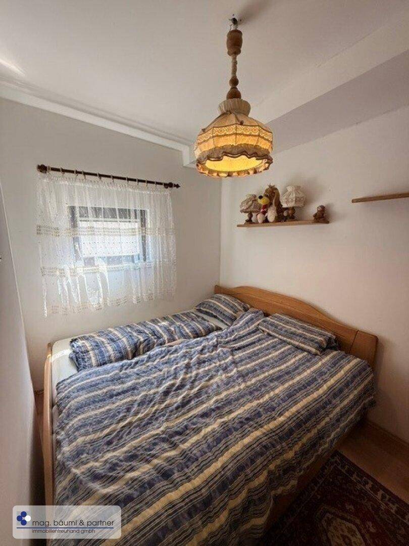 Schlafzimmer mit Doppelbett, Holzbettrahmen und einem kleinen Fenster.