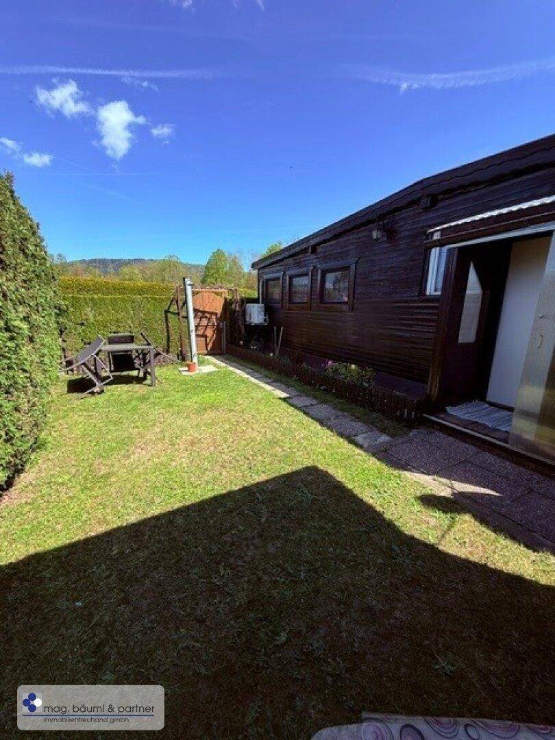 Gepflegter Gartenbereich mit Rasenfläche, Hecke und Gartenmöbeln neben dem Haus.