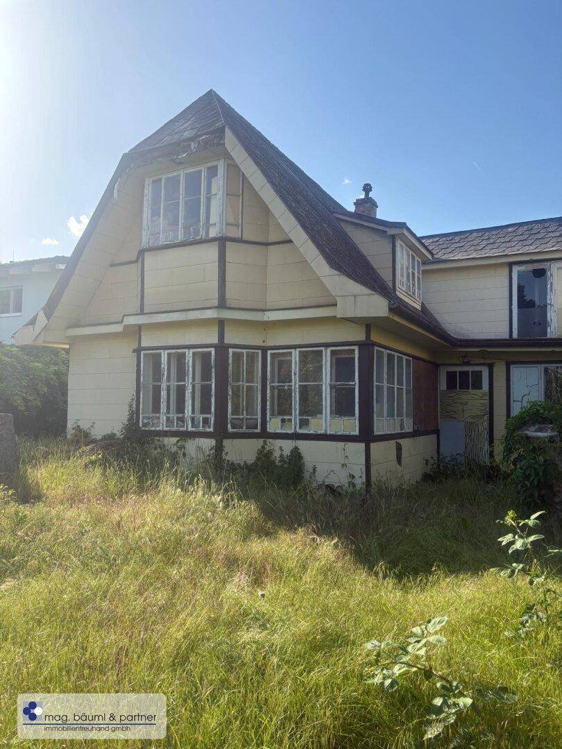 Verwahrlostes Haus mit verwitterter Fassade und überwuchertem Gartenbereich bei Sonnenschein.
